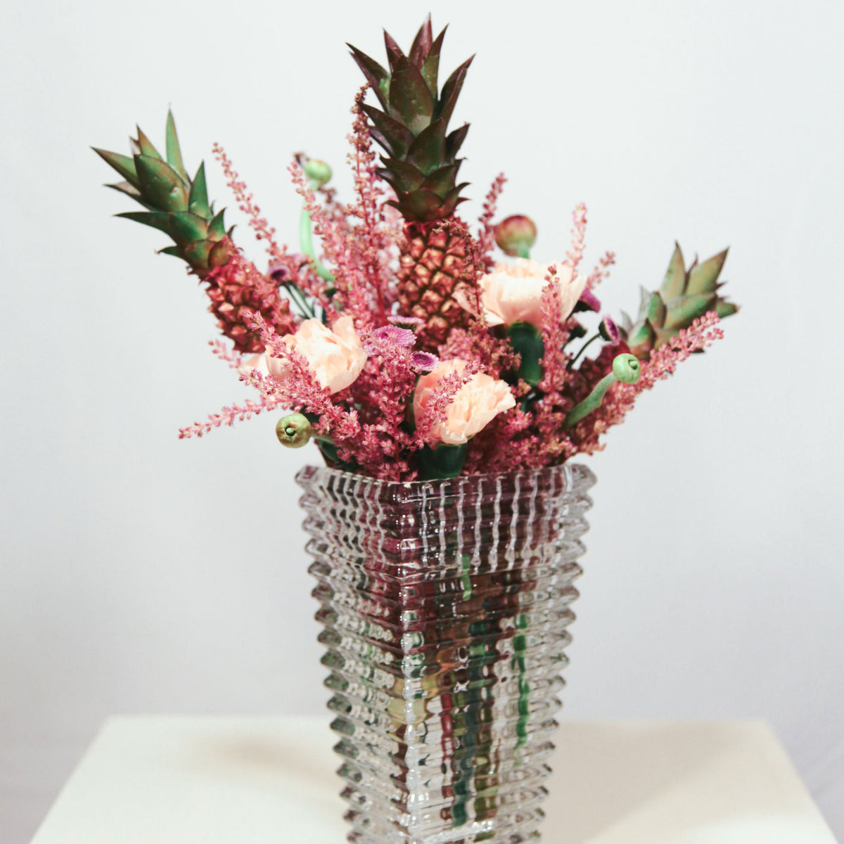 Vase with pink flowers and pineapples on a white surface small arregment 