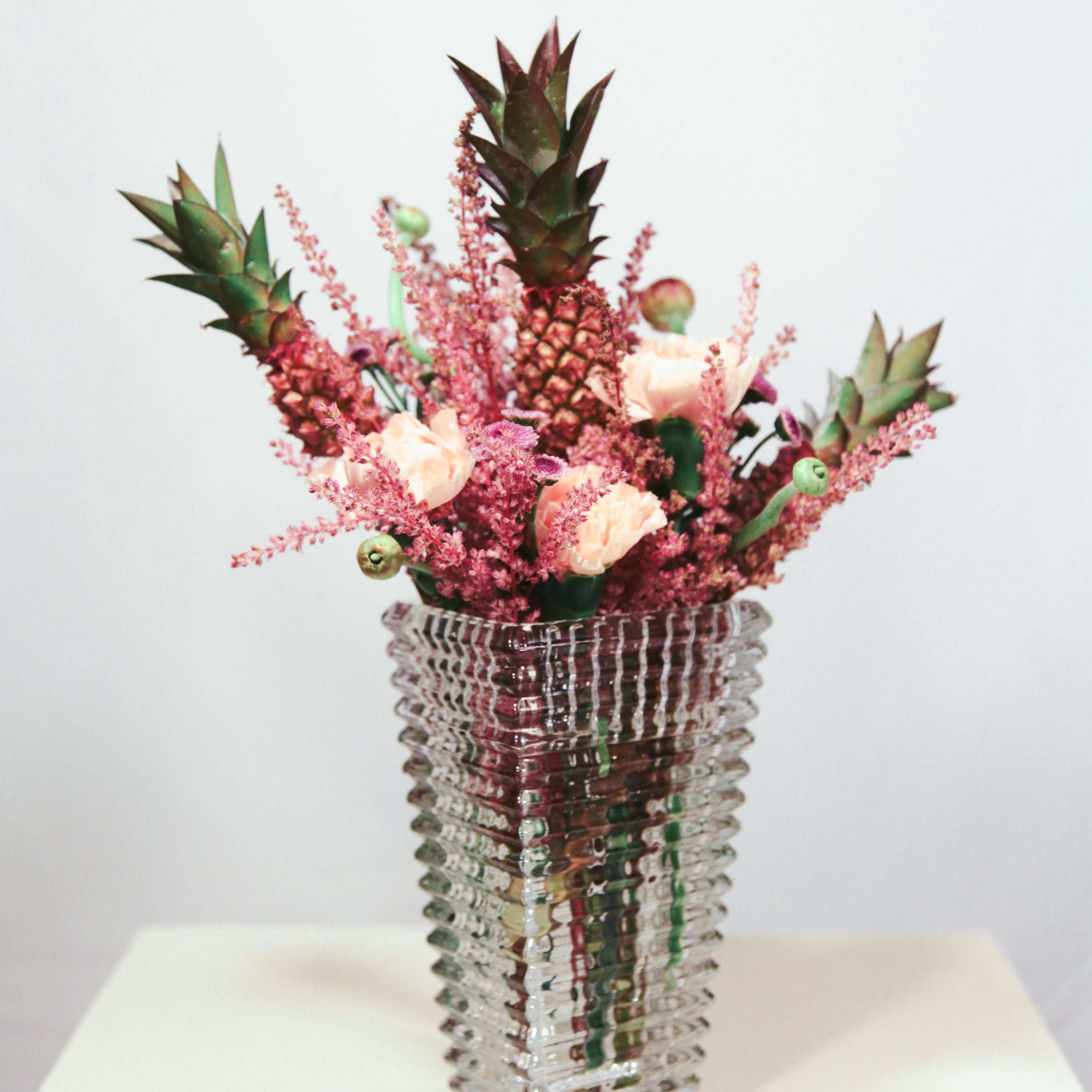 Vase with pink flowers and pineapples on a white surface small arregment 